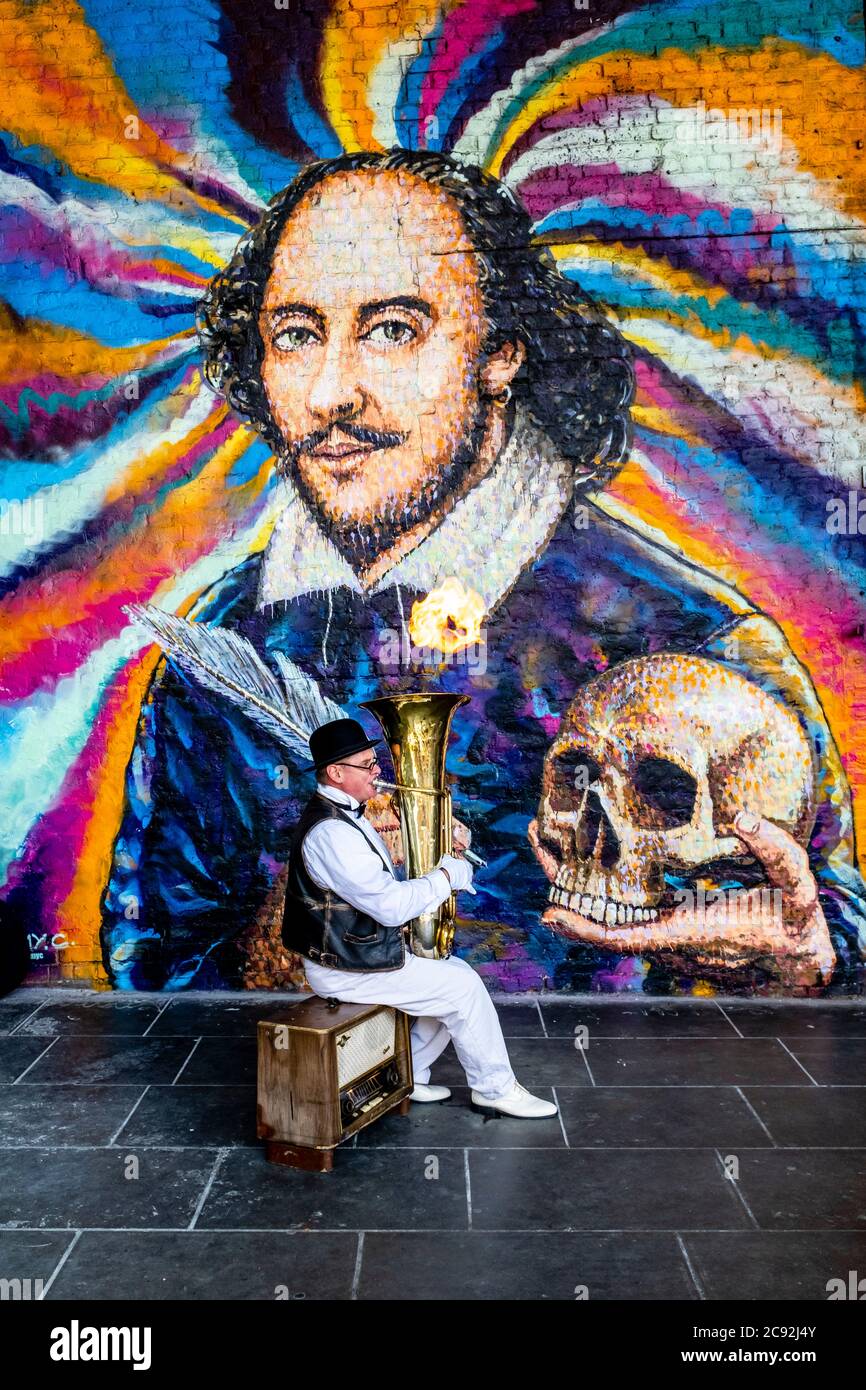 Ein Street Entertainer spielt Musik vor EINEM riesigen Wandbild von William Shakespeare, Clink Street, London, Großbritannien Stockfoto