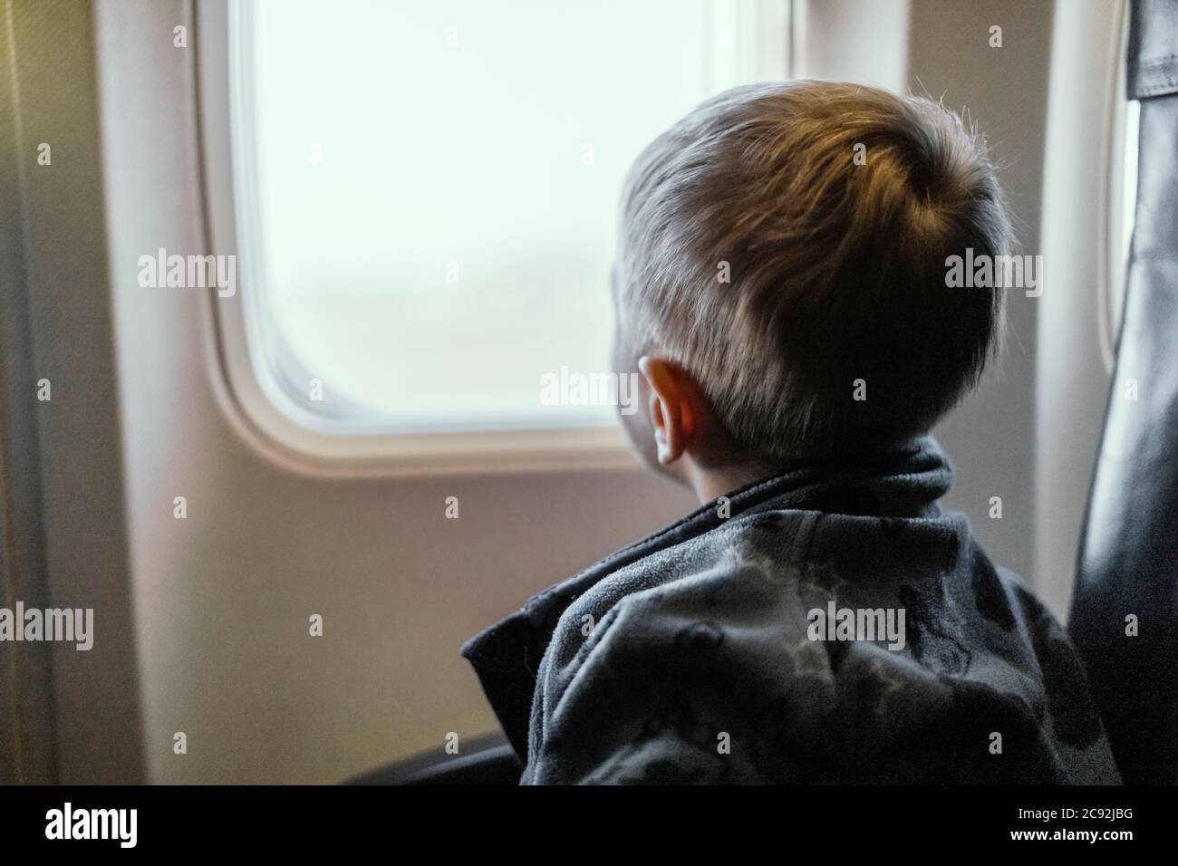 Ein kleiner blonder Junge, der durch das Fenster im Flugzeug schaut Stockfoto