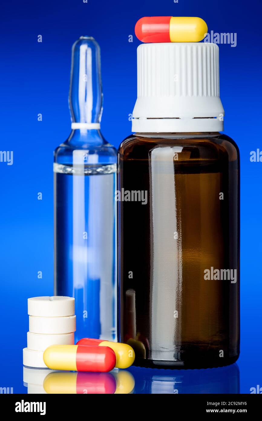 Hustensirup mit einer Ampulle für einen Impfstoff, Glasflasche mit einer gelb-roten Pille und runde Tabletten auf Glas mit blauem Hintergrund, niemand. Stockfoto