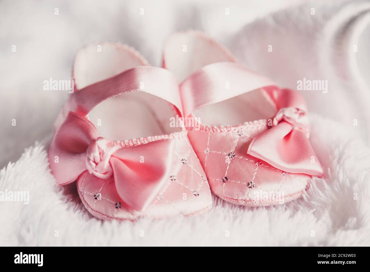 Kleidung für Neugeborene. Ein Paar niedliche babyrosa Schuhe mit Schleife für Mädchen auf einem weißen Bett. Stockfoto