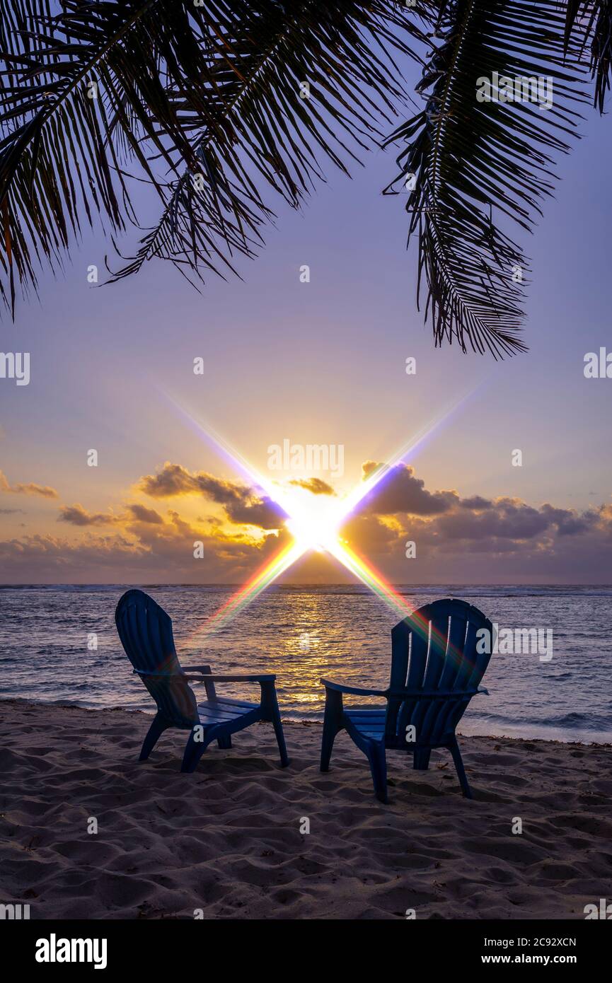 Sonnenuntergang mit Sonneneinstrahlung, Strandliegen und Palmen. Grand Cayman Island Stockfoto