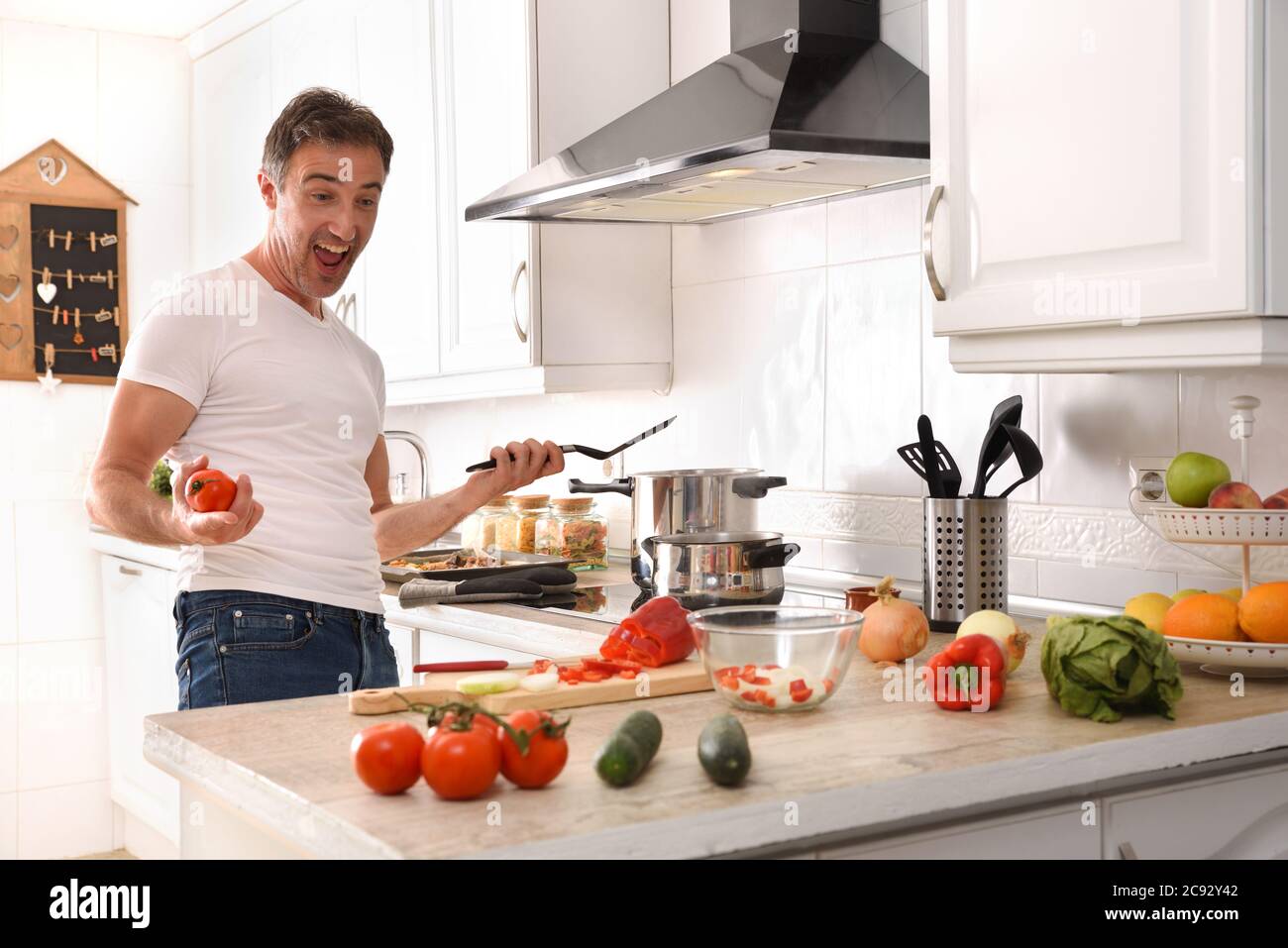 Glücklicher und ausdrucksstarker Mann, der gerne Gemüse zu Hause in einer Wohnküche kocht Stockfoto