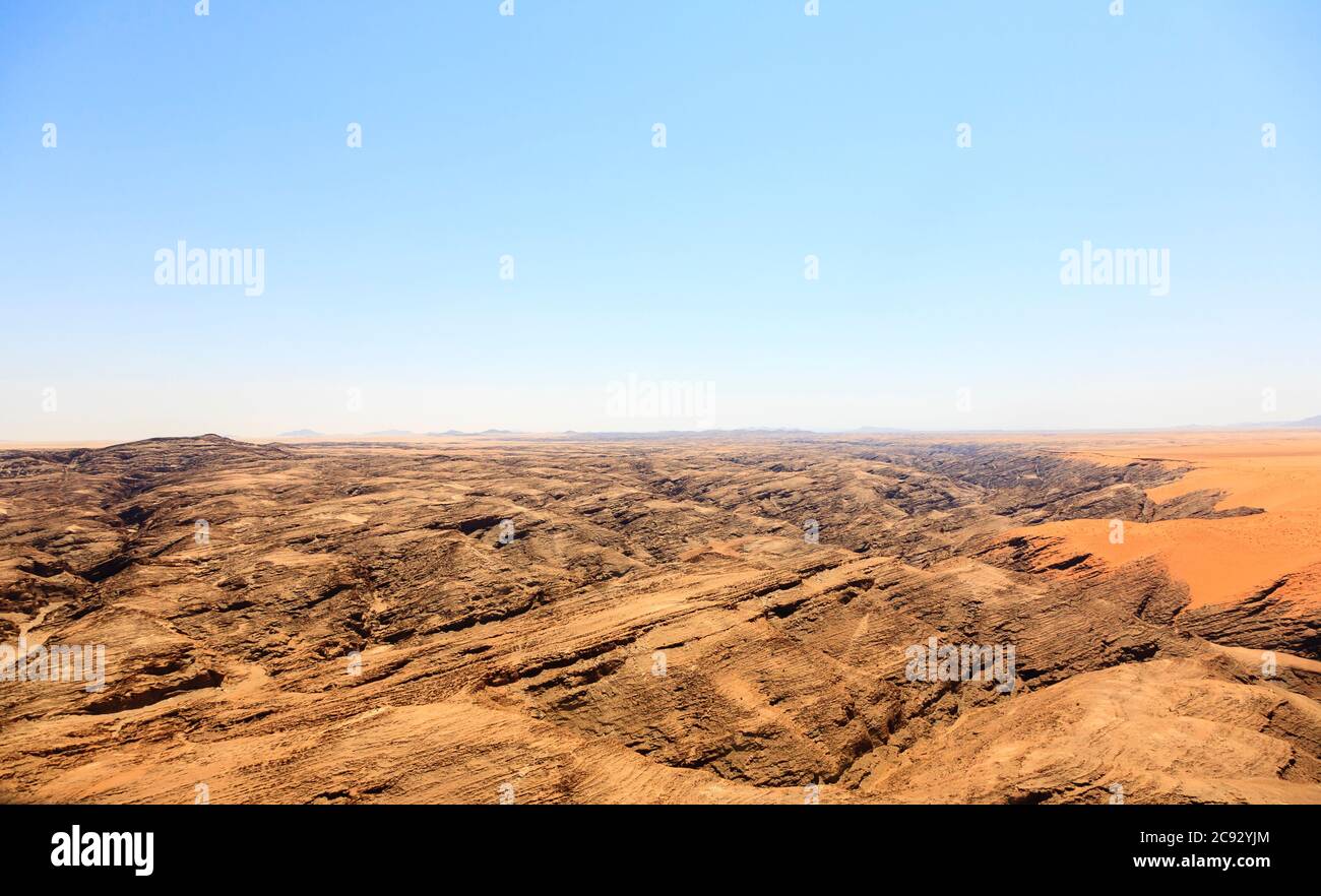 Typisches trostiges, arides Berggebiet der Namib-Wüste mit ockerfarbenem Sand auf geschichteten Felsen an der Skelettküste, Namibia, Südwestafrika Stockfoto