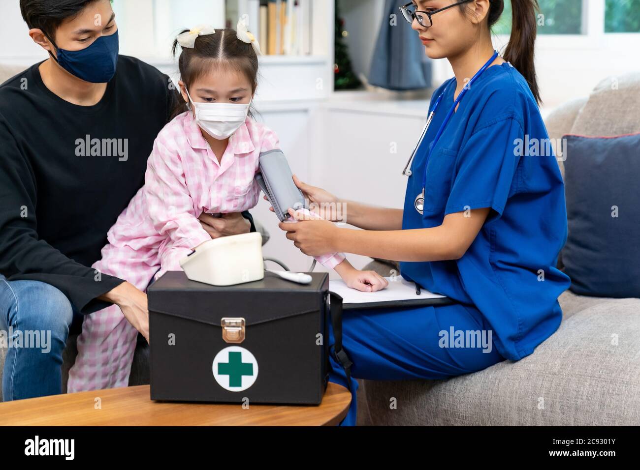 Asiatische Arzt nehmen Blutdruck-Messung zu kleinen Mädchen Kind sitzen mit ihrem Vater im Wohnzimmer, während Arzt zu Hause besuchen. Versorgung im häuslichen Gesundheitswesen Stockfoto