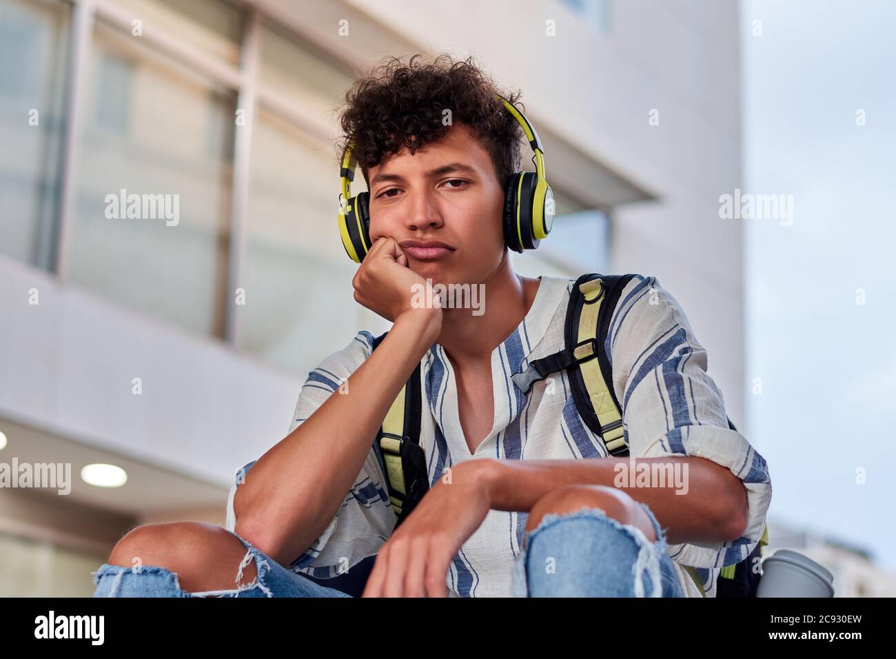 Langweiliger junger Afro mit Kopfhörern auf der Straße sitzend Stockfoto