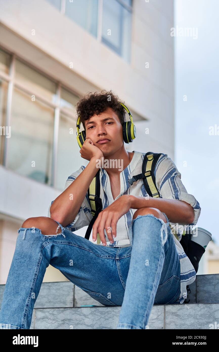 Langweiliger junger Afro mit Kopfhörern auf der Straße sitzend Stockfoto