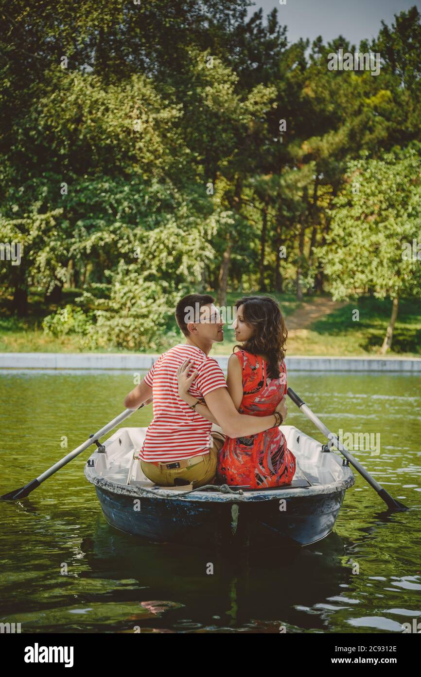 Junge schöne glücklich liebende Paar rudern ein kleines Boot auf einem See. Ein lustiges Date in der Natur. Ein Paar umarmt sich in einem Boot. Stockfoto