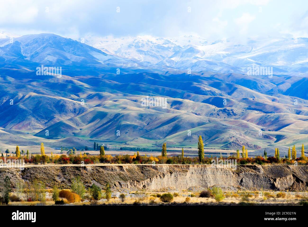 Landschaft Kirgisistans in der Region Issyk Kul. Grasland mit schneebedeckten Bergen der Tian Shan Bergkette teilweise hinter Wolken gesehen. Stockfoto
