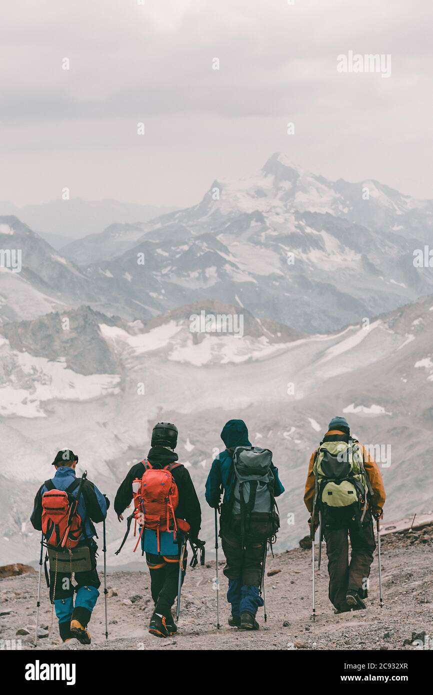 Wandern und Klettern. Vier Touristen mit Rucksäcken auf dem Hintergrund eines schneebedeckten Bergrückens. Stockfoto