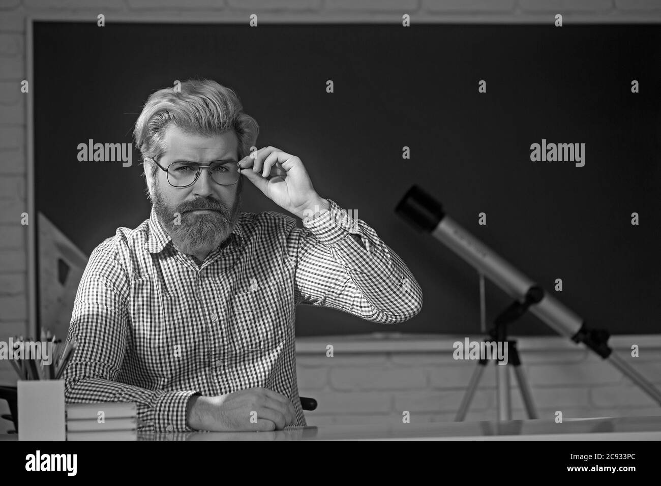 Der junge Professor hält einen Stapel Bücher und schaut über seine Brille. Stockfoto