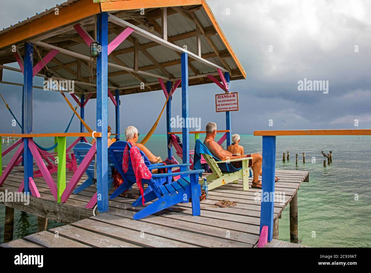 Westliche ältere Touristen in Strandliegen mit Blick auf das Karibische Meer von einem hölzernen Steg auf Caye Caulker / Cayo Caulker, Insel vor der Küste von Belize Stockfoto