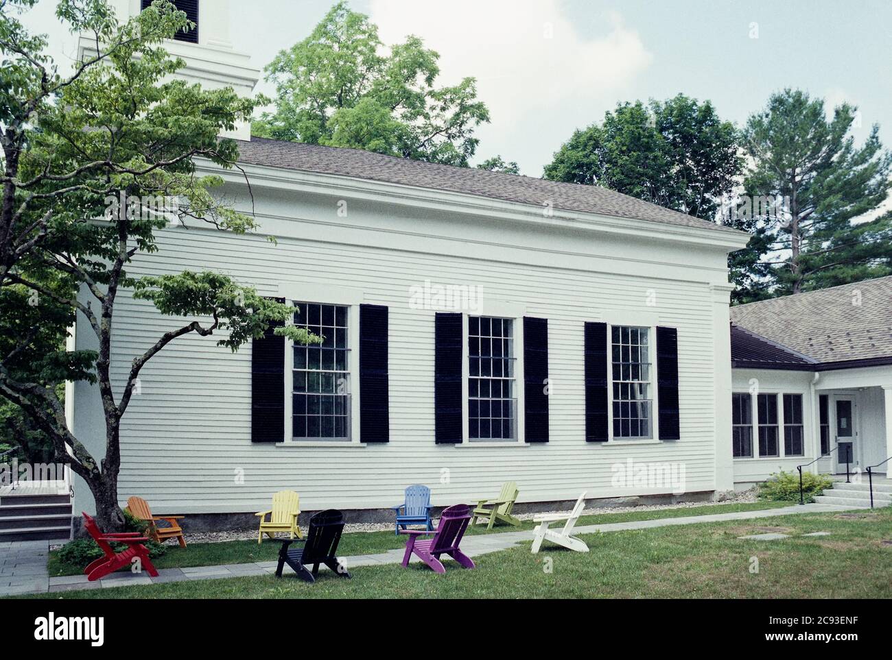 Bunte Adirondack Stühle sitzen leer, sechs Meter auseinander für soziale Distanzierung außerhalb einer weißen New England Kirche in der Sommersonne. Die Distanzierung Stockfoto