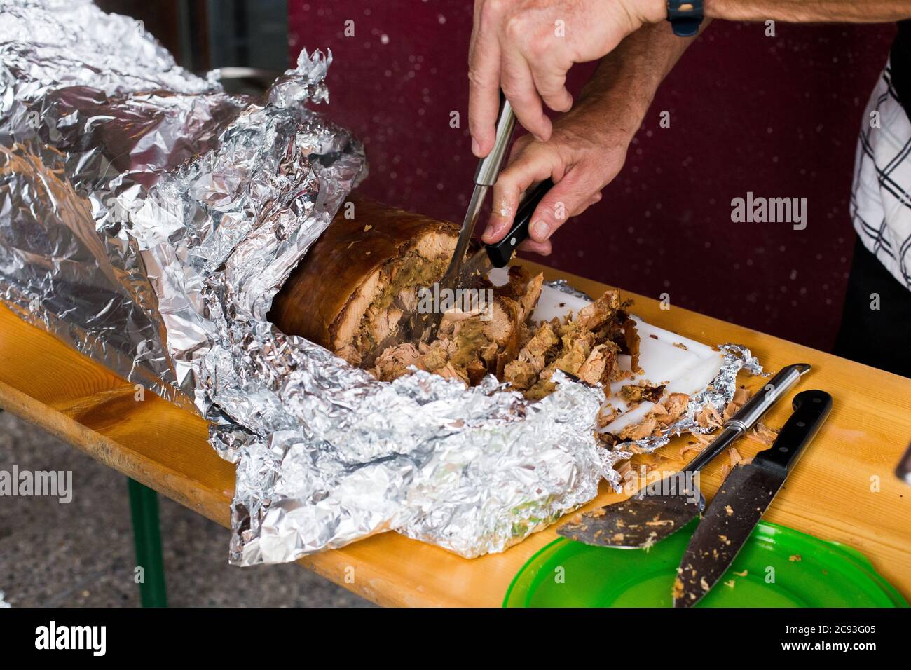 Gegrilltes Ferkel / Spanferkel, mit der Haut noch darauf in Aluminiumfolie eingewickelt. Eine Person schneidet und serviert. Stockfoto