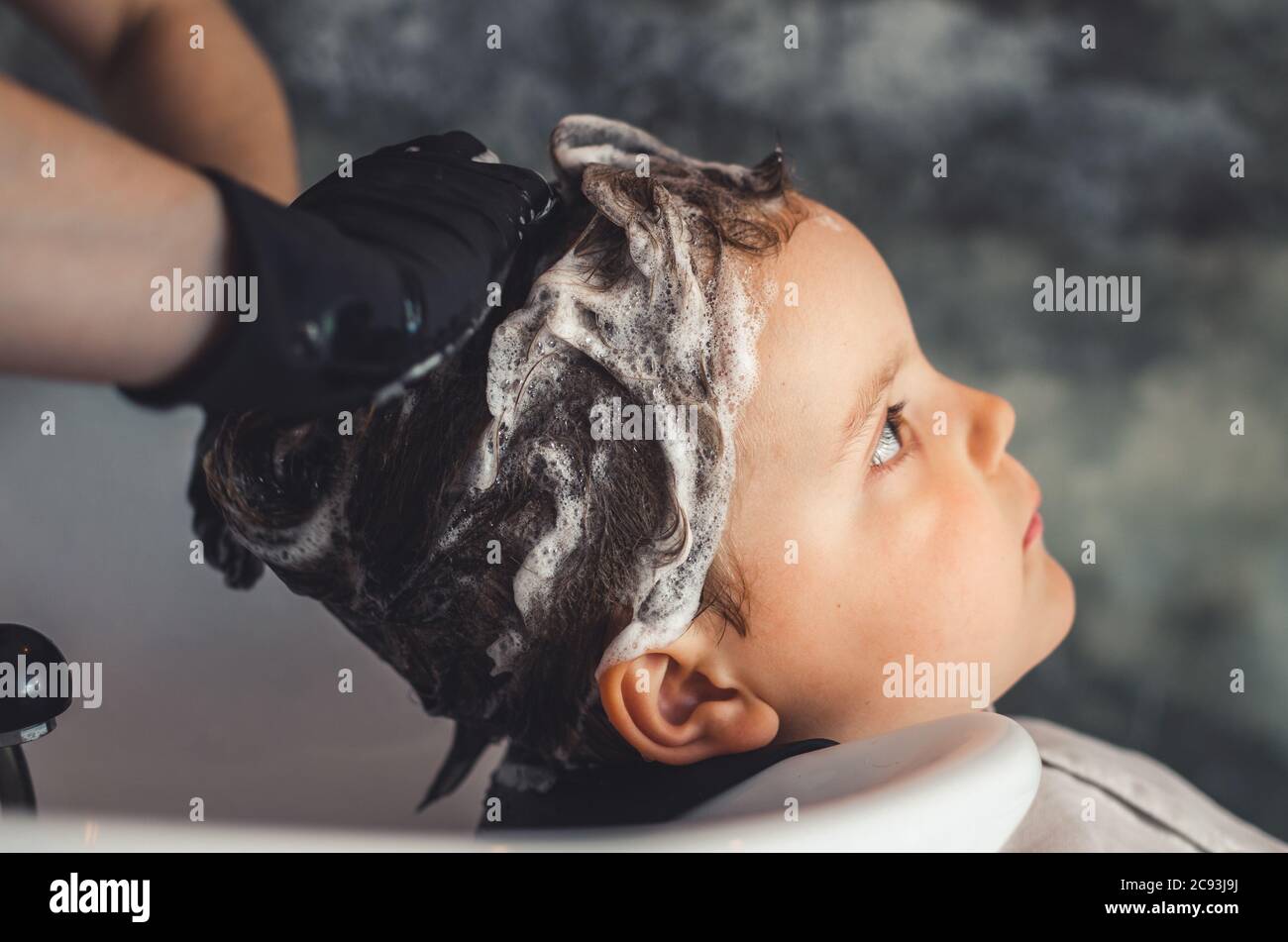 Hände eines Friseurs mit schwarzen Latexhandschuhen, die die Haare eines Kindes waschen Stockfoto