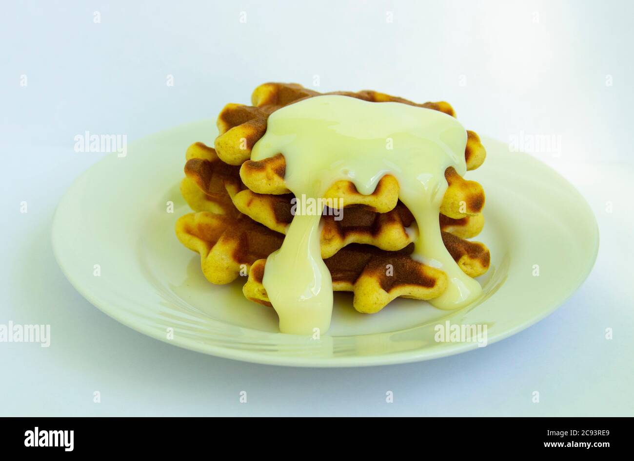 Gebackene Waffeln mit weißem Teller und weißem Teller. Bedeckt mit weißer Süßcreme. Stockfoto