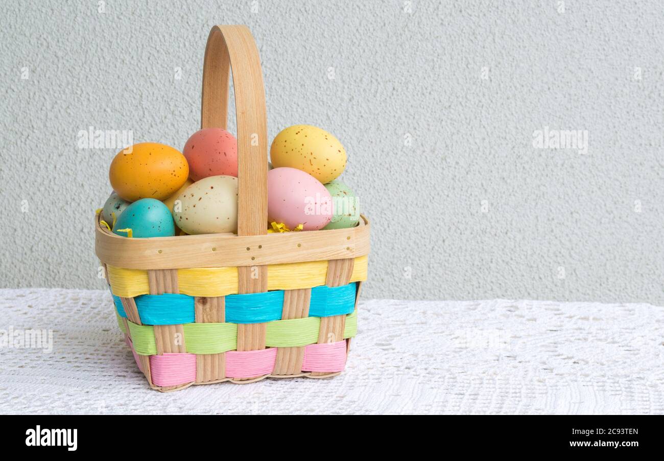 Ein kleiner Korbkorb mit Pastellfarben gesprenkelten Ostereiern auf einer Tischdecke aus Spitze mit Kopierfläche Stockfoto