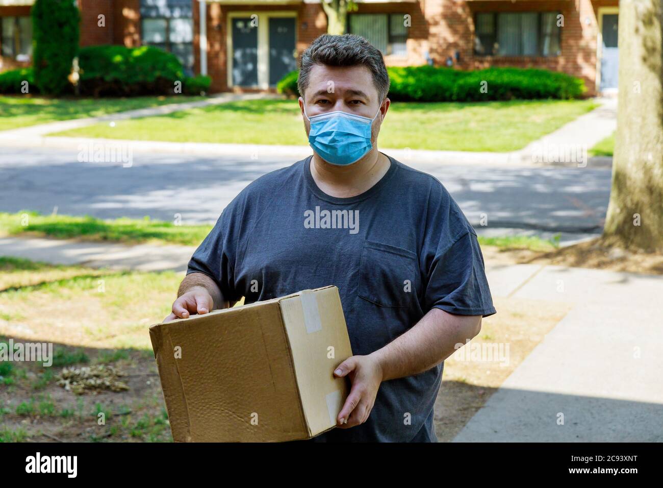Hauszustellung, online bestellen ein Mann in einer medizinischen Maske mit einem Karton, ein Paket in den Händen Lebensmittelzustellung während der Quarantäne der Coronavirus-Pandemie. Stockfoto