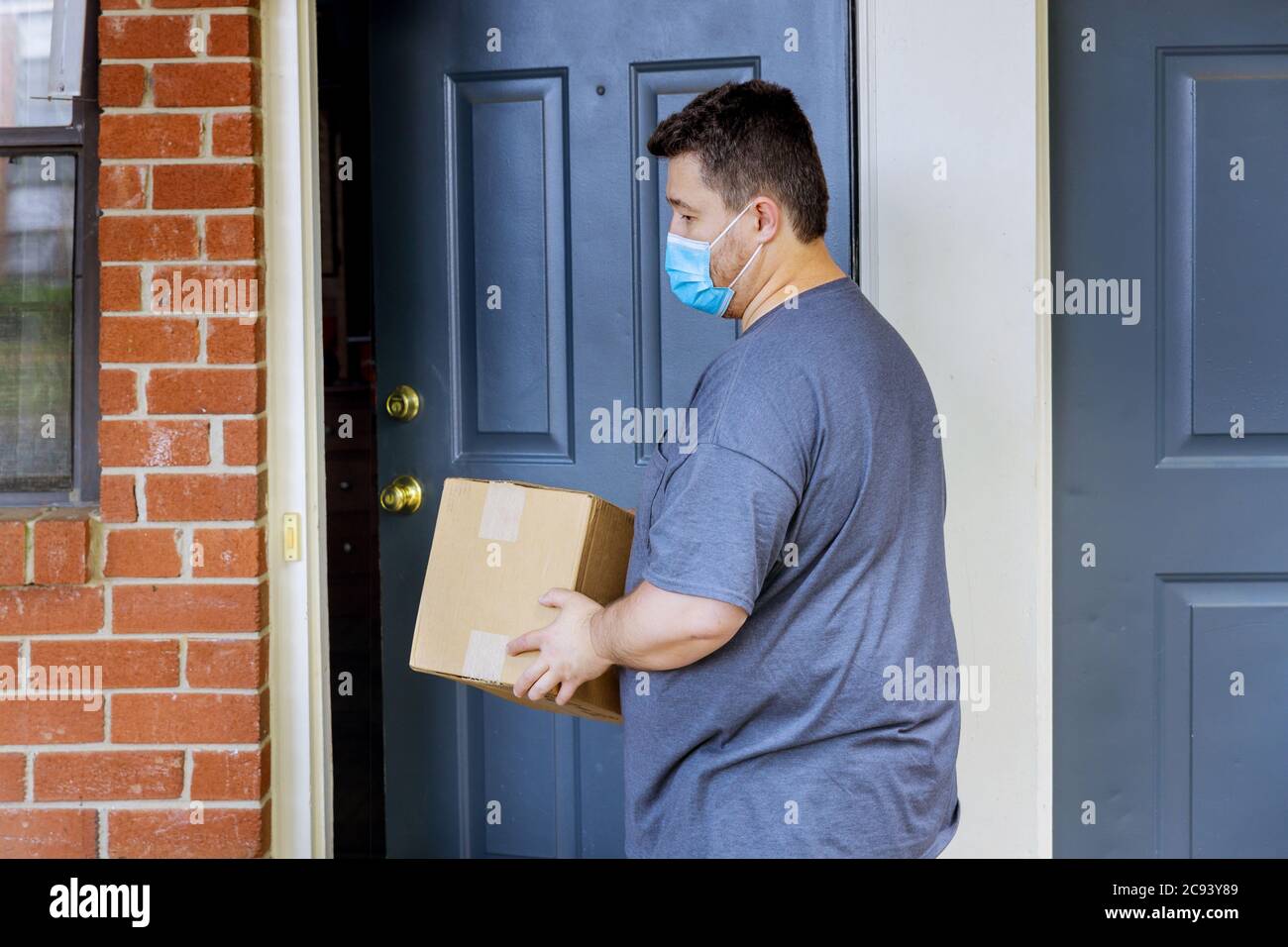 Home online bestellen Lieferung von Lebensmitteln während der Quarantäne der Coronavirus-Pandemie ein Mann in einer medizinischen Maske mit Box Paket in den Händen Stockfoto