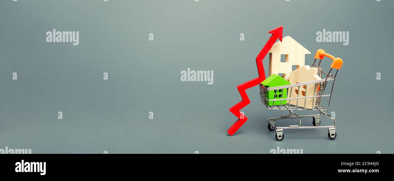 Holzhäuser in einem Einkaufswagen und roter Pfeil nach oben. Konzept für das Preiswachstum bei Immobilien. Hohe Nachfrage nach Wohnraum. Gebäudewartung. Sinkende Marktratte Stockfoto