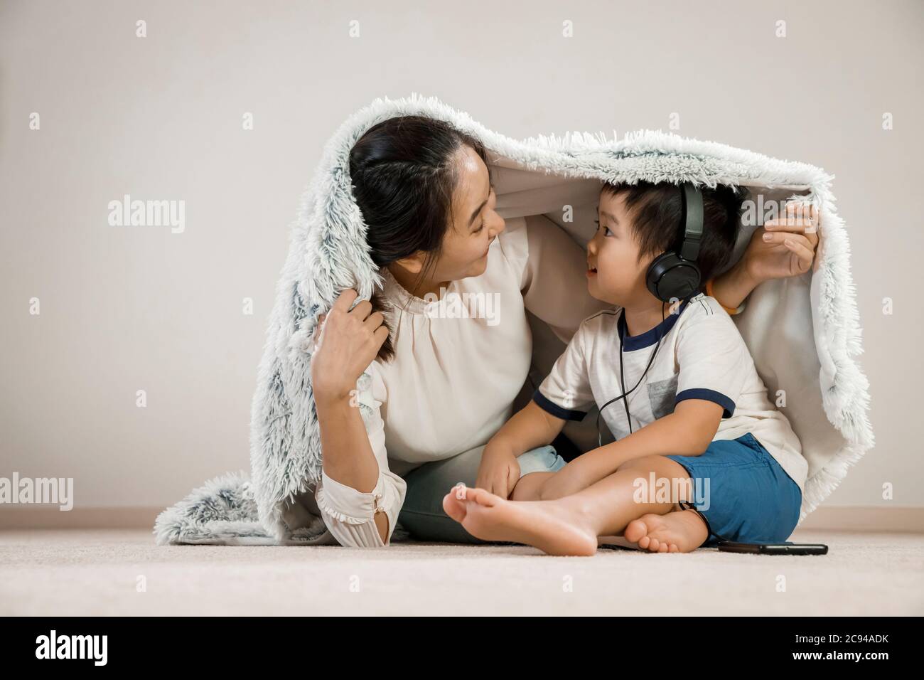 Asiatische Mutter versteckt unter Decke mit Kleinkind Kopfhörer tragen. Vietnamesische Mutter lächelt spielen verstecken und suchen mit ihrem Sohn, Familie Zeit Konzept Stockfoto