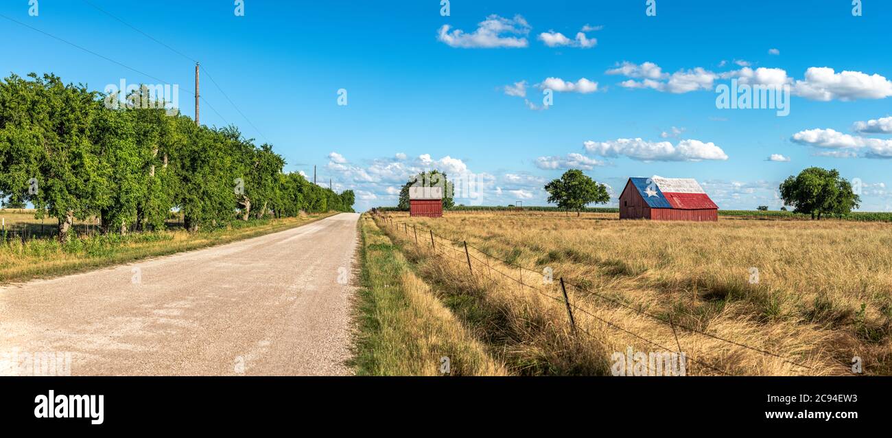 Eine verlassene alte Scheune in Rural Texas mit der Staatsflagge auf dem Dach sitzt in einer Farmland-Gemeinschaft, die von Feldern und einer Feldstraße eingerahmt ist. Stockfoto
