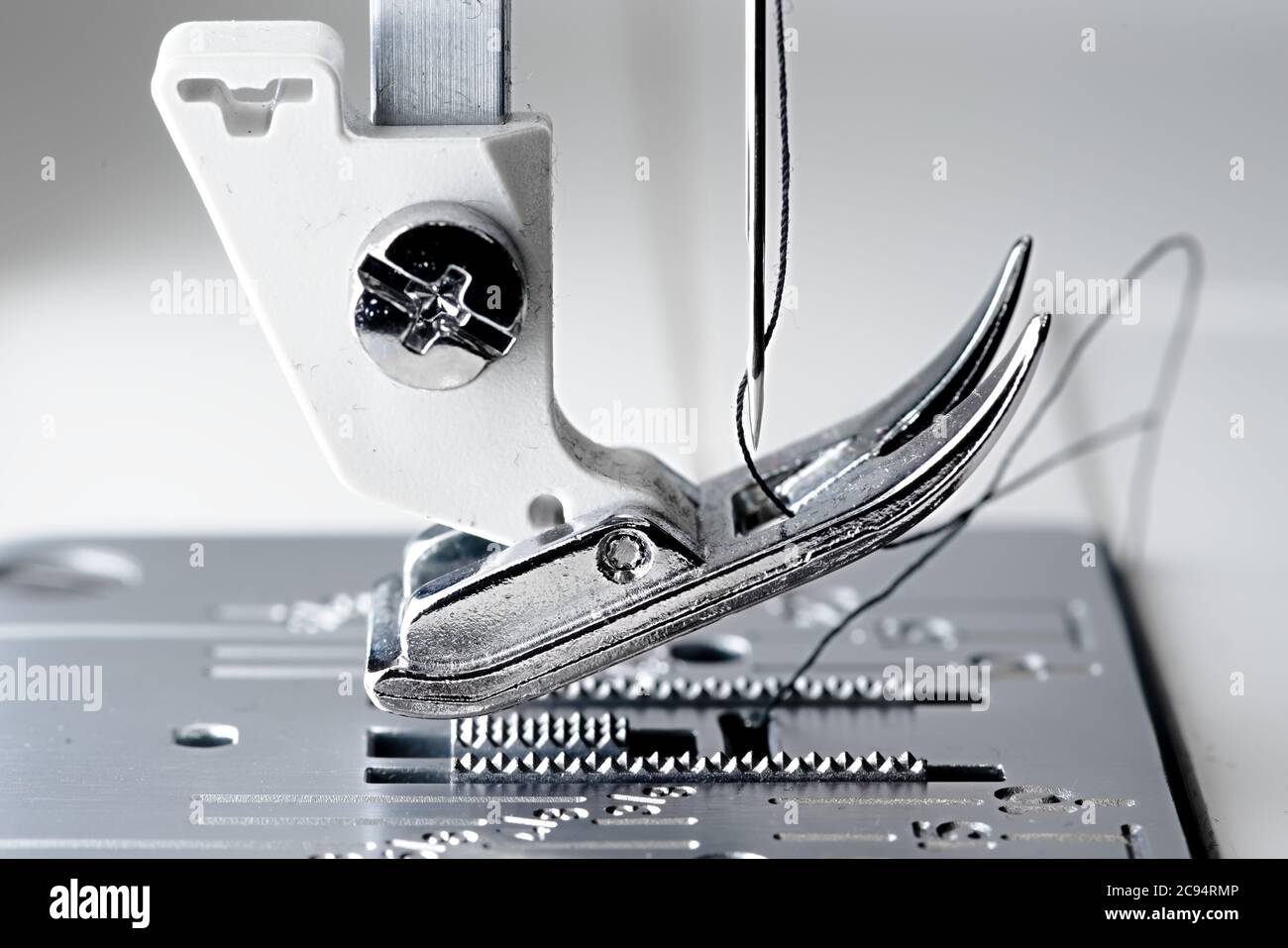 4 - Super Makro-Bild mit selektivem Fokus auf Nadel und Faden. Zeigt den Mechanismus und Arbeitsbereich einer weißen und metallenen Nähmaschine. Stockfoto