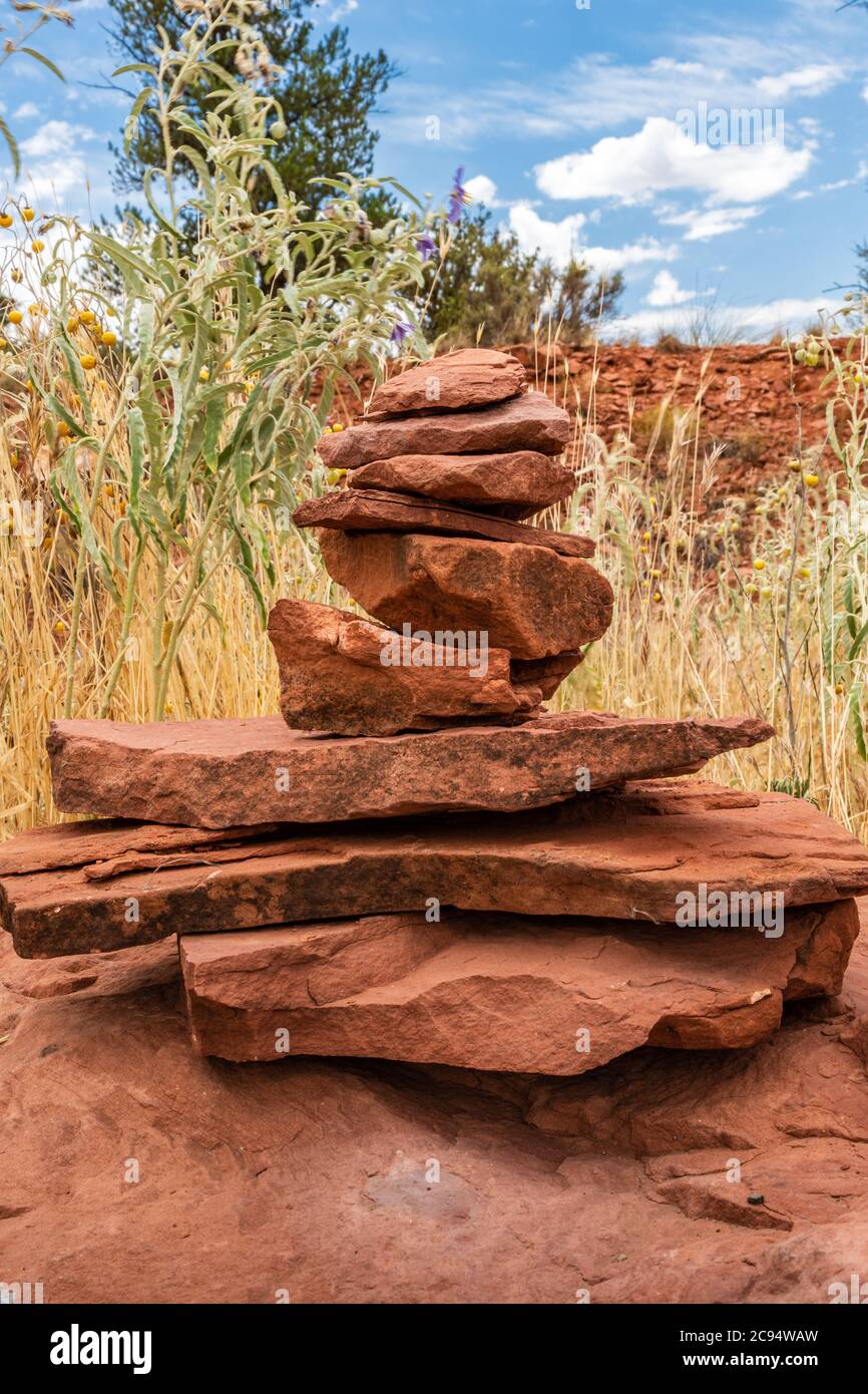 Balance und Wellness-Konzept. Nahaufnahme eines Stapels roher roter Felsen mit Wüstenpflanzen im Hintergrund. Stockfoto