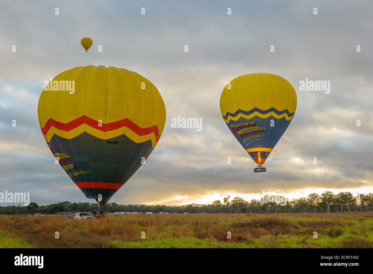 Als die Sonne aufgeht, beginnen drei bunte Luftballons mit Touristenkörben ihren Abenteuerflug über Mareeba in Queensland, Australien. Stockfoto