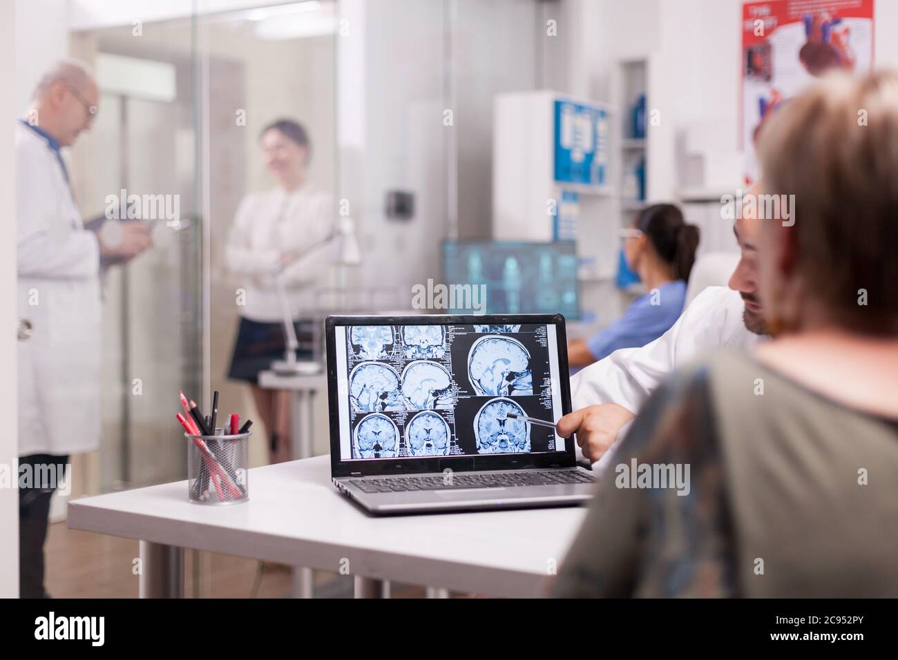 Ältere Frau im Krankenhausbüro, die Gehirn CT-Scan beim Gespräch mit dem Arzt über die Diagnose. Kranke junge Frau und ältere Sanitäter mit grauen Haaren im Klinikkorridor. Stockfoto
