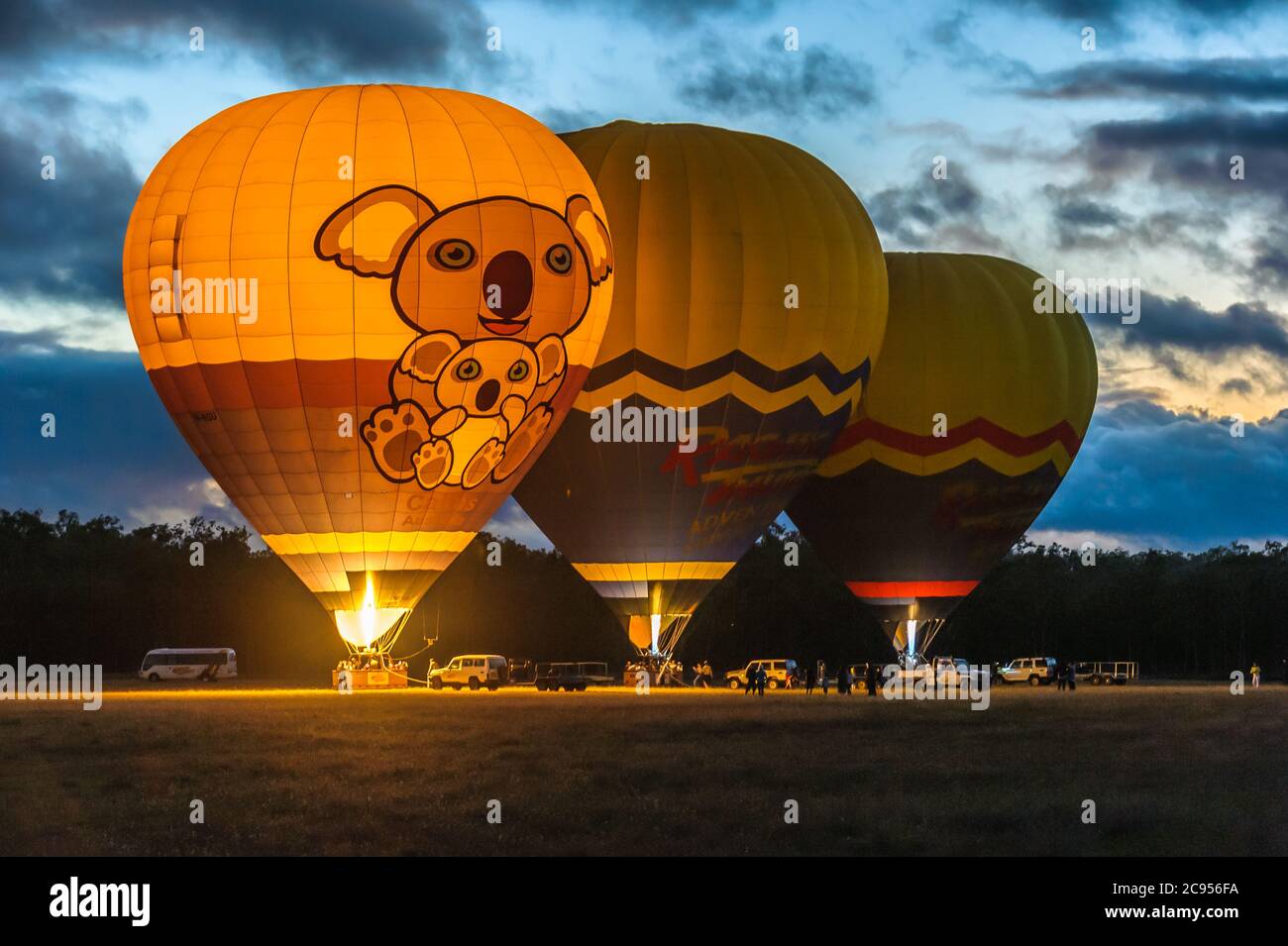 Als die Sonne aufgeht, starten drei bunte Ballons mit touristisch gefüllten Körben zu einem Flug über Mareeba in Queensland, Australien. Stockfoto