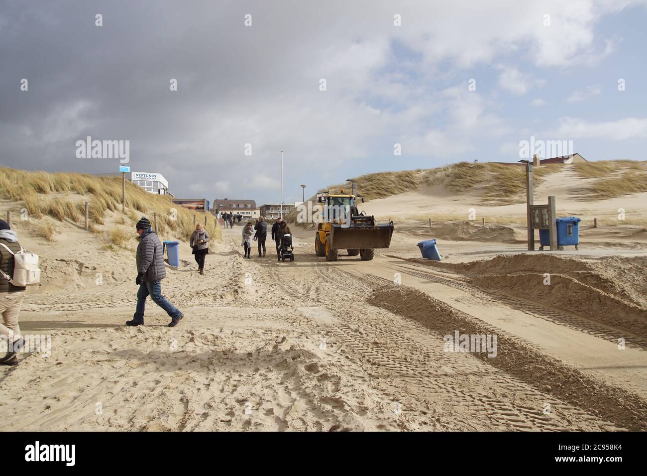 Eine Planierraupe schiebt den Sand am Eingang zum Strand von Bergen aan Zee. Viel Wind. Niederlande, März Stockfoto