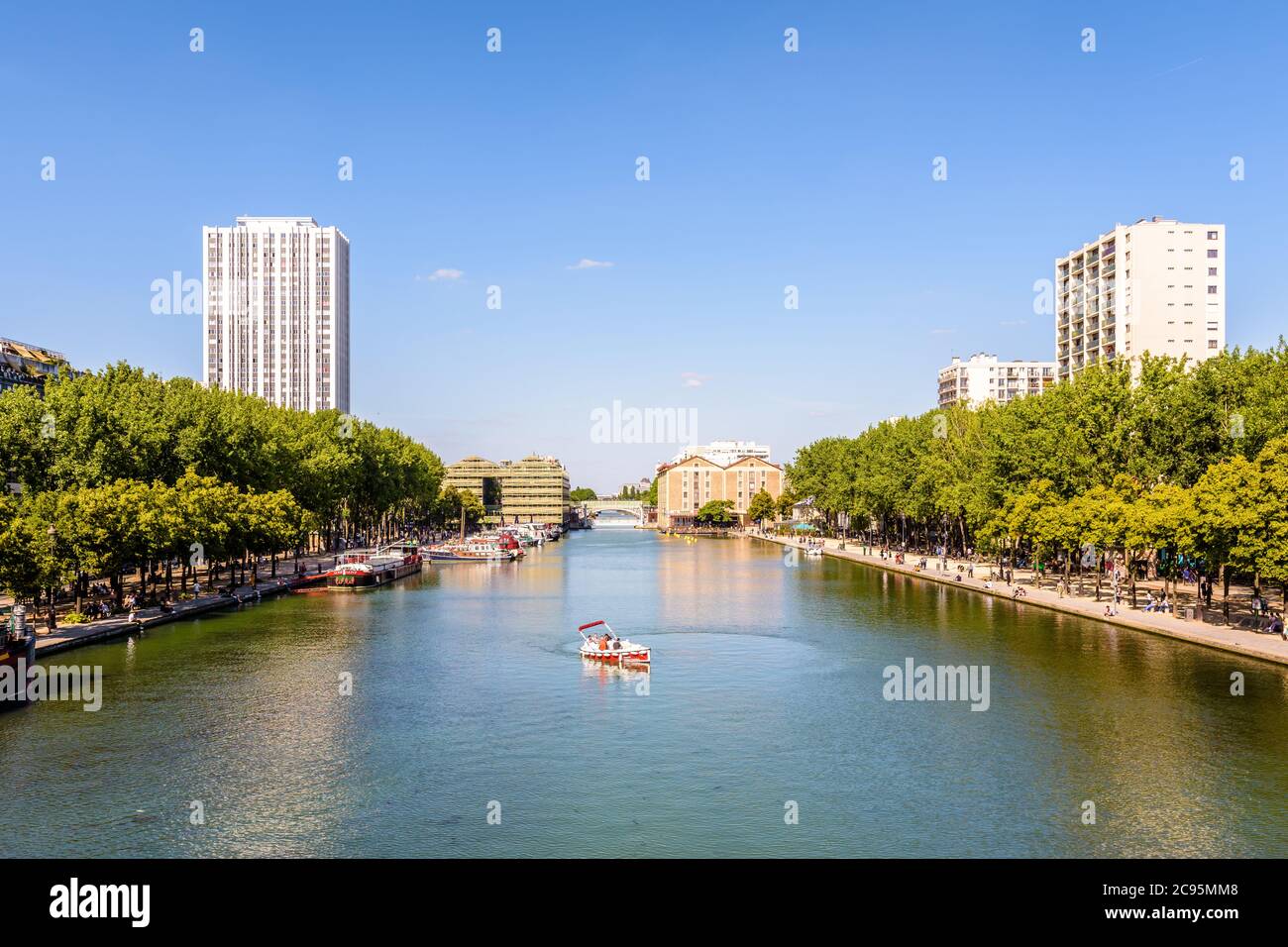 Menschen genießen eine Tour an Bord eines elektrischen Mietbootes auf La Villette Becken in Paris, Frankreich, mit den beiden ehemaligen Lagerhäusern im Hintergrund. Stockfoto