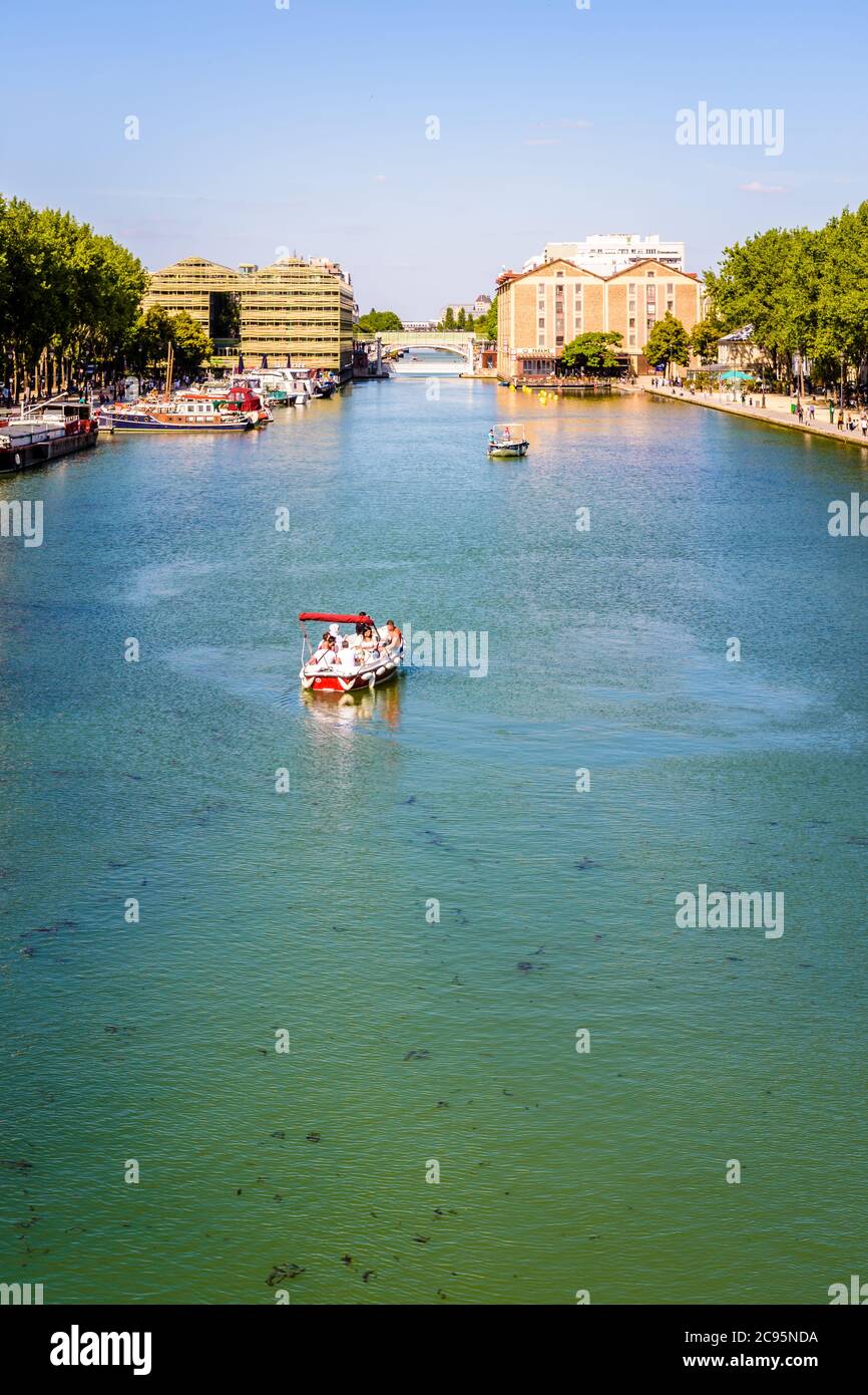 Menschen genießen eine Tour an Bord eines elektrischen Mietbootes auf La Villette Becken in Paris, Frankreich, mit den beiden ehemaligen Lagerhäusern im Hintergrund. Stockfoto