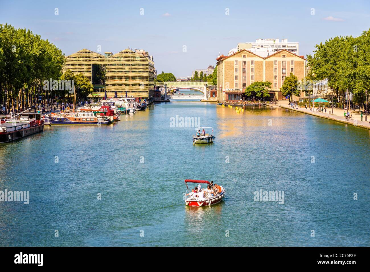 Menschen genießen eine Tour an Bord eines elektrischen Mietbootes auf La Villette Becken in Paris, Frankreich, mit den beiden ehemaligen Lagerhäusern im Hintergrund. Stockfoto