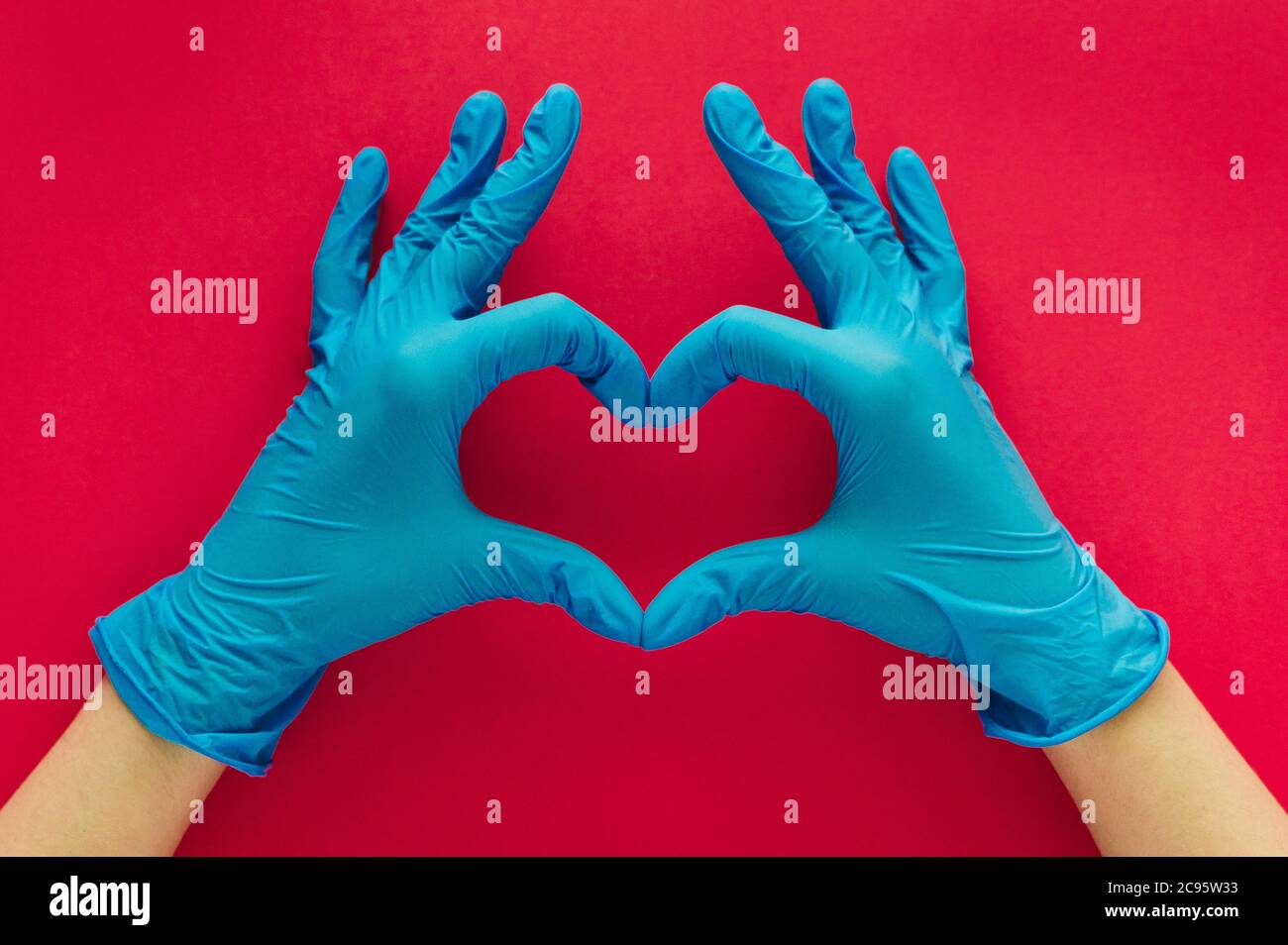Stock Foto einer Frau Hände mit blauen Handschuhen bilden ein Herz mit ihren Fingern auf einem roten Hintergrund Stockfoto