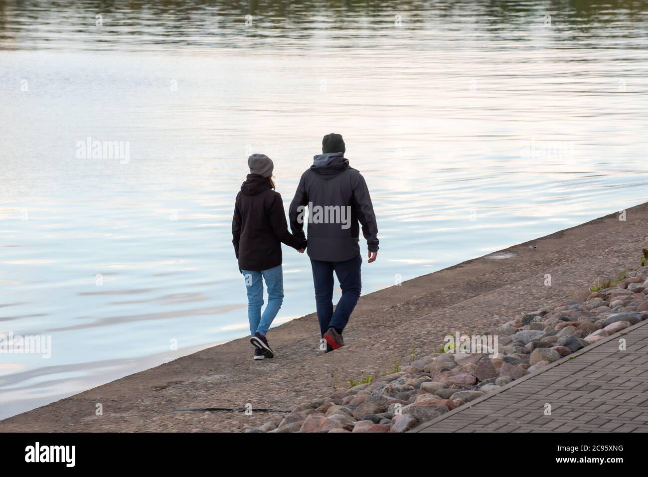 Rückansicht eines glücklichen jungen Paares in der Liebe halten Hände zu Fuß entlang der Stadt Flussufer Stockfoto
