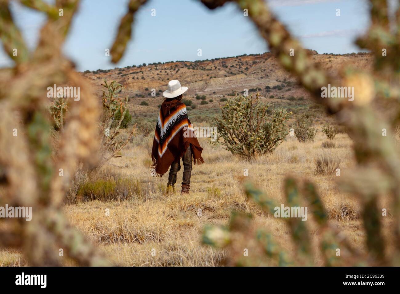 Hispanic Frau in einem Poncho und Cowboy Hut Wanderungen durch eine dramatische, heiße Wüstenlandschaft umgeben von hohen Kakteen in der ojito Wildnis Gegend, New M Stockfoto