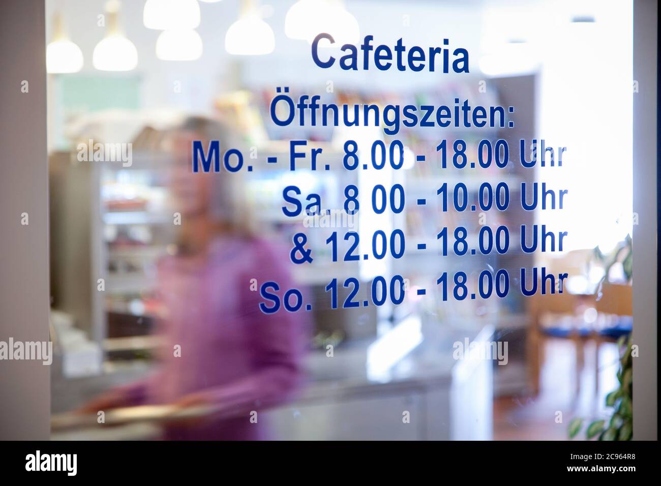 Essen, Nordrhein-Westfalen, Deutschland - Klinikcafeteria. Glastür mit den Öffnungszeiten. Im Hintergrund sind Leute mit Tabletts walki Stockfoto