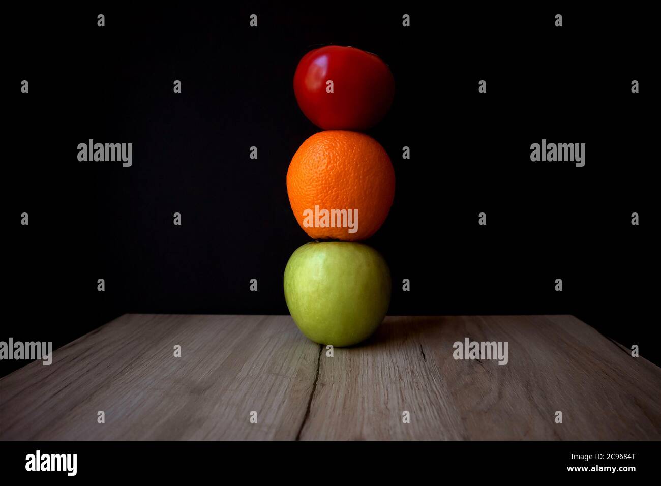 Komposition aus reifen Tomaten, grünem Apfel und Orange übereinander auf einem Holzbrett gestapelt Stockfoto