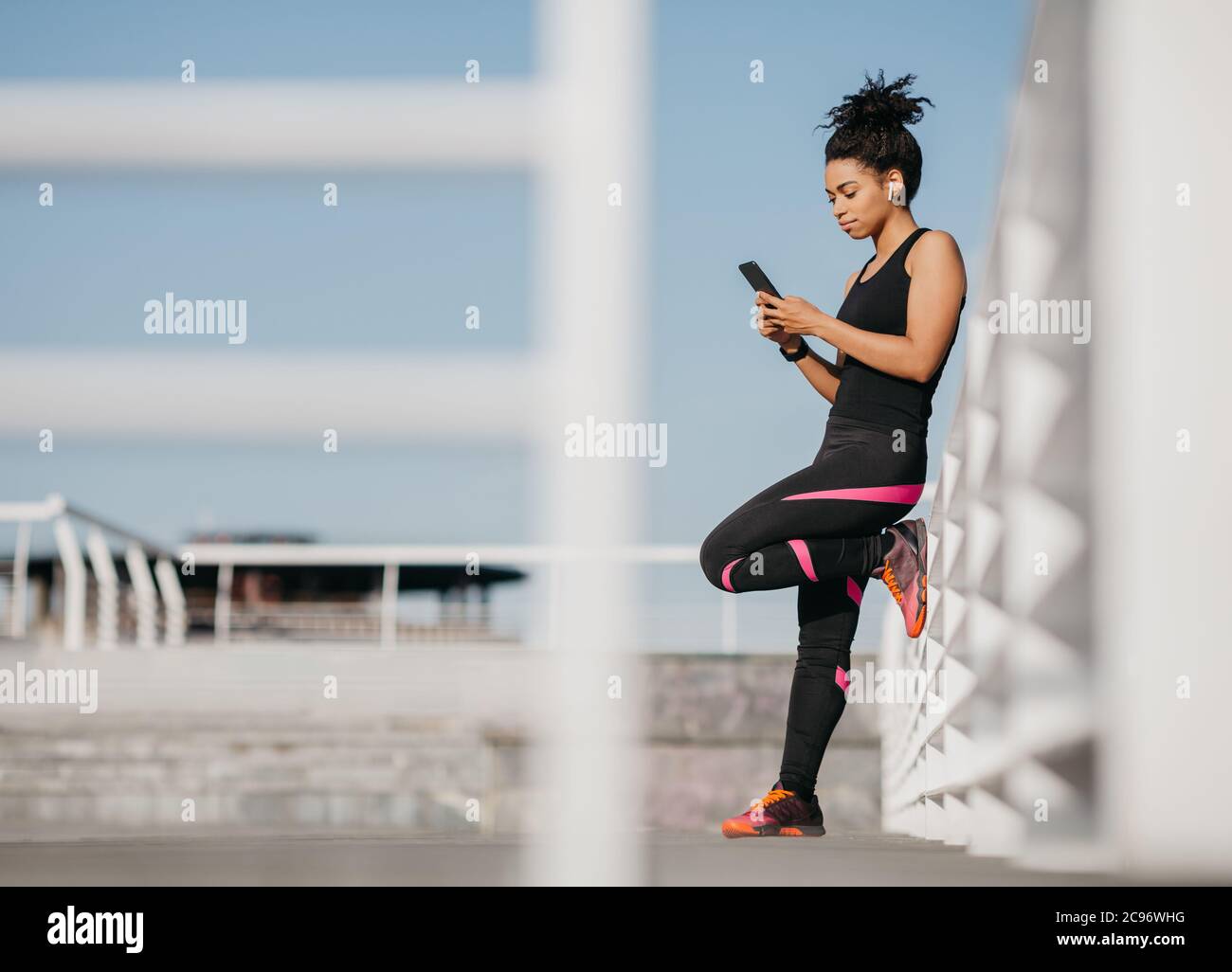 Sport-Blog und Outdoor-Workout. Serious african american Mädchen in Mode Sportbekleidung mit kabellosen Kopfhörern, Eingabe auf Smartphone Stockfoto