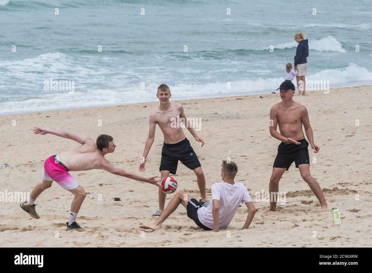 Eine Gruppe von Burschen, die in einem Kurzurlaub am Fistral Beach in Newquay in Cornwall mit einem Ball spielen. Stockfoto
