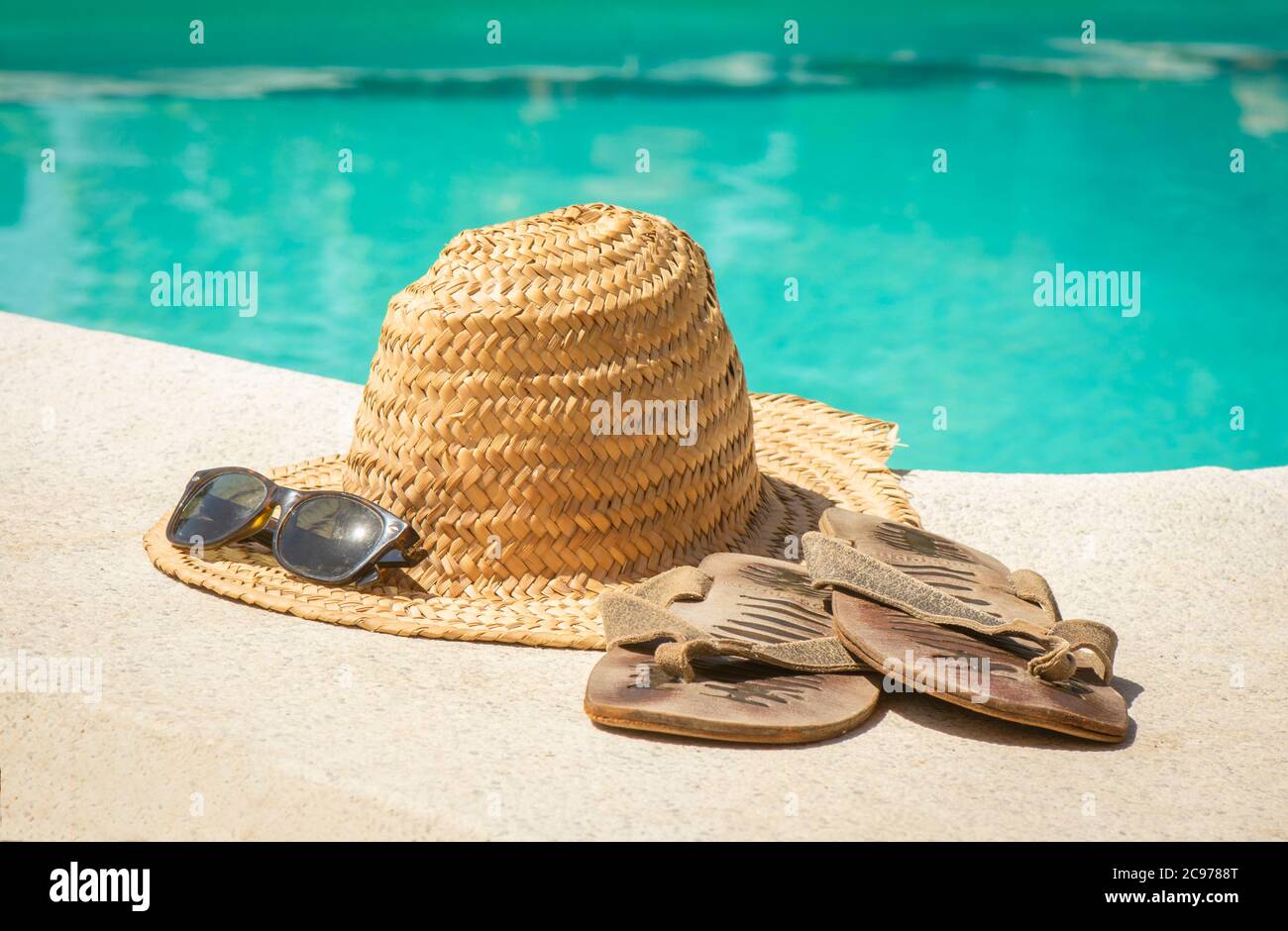Vintage Strohhut mit Sonnenbrillen und Flip Flops am Rand eines Schwimmbades. Stockfoto