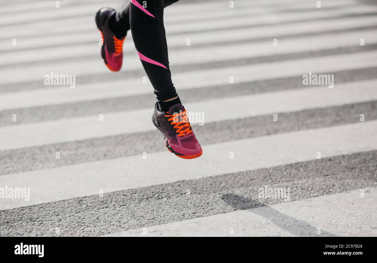 Springt und friert in der Luft ein. Mädchen in Sportswear und Sneakers läuft entlang Übergang entlang der Straße Stockfoto