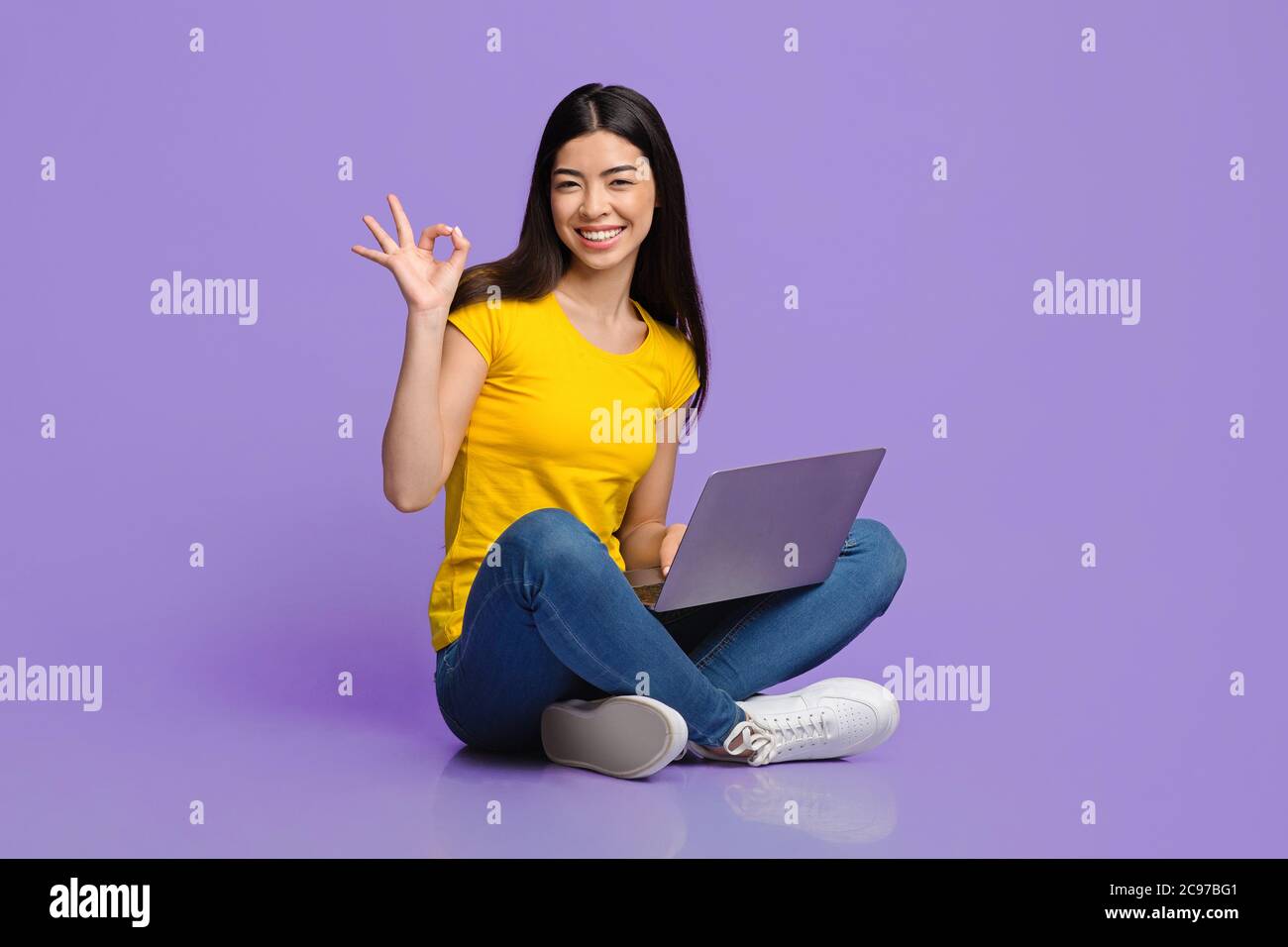 Alles in Ordnung. Fröhlich asiatische Mädchen sitzen mit Laptop und zeigt okay Zeichen Stockfoto