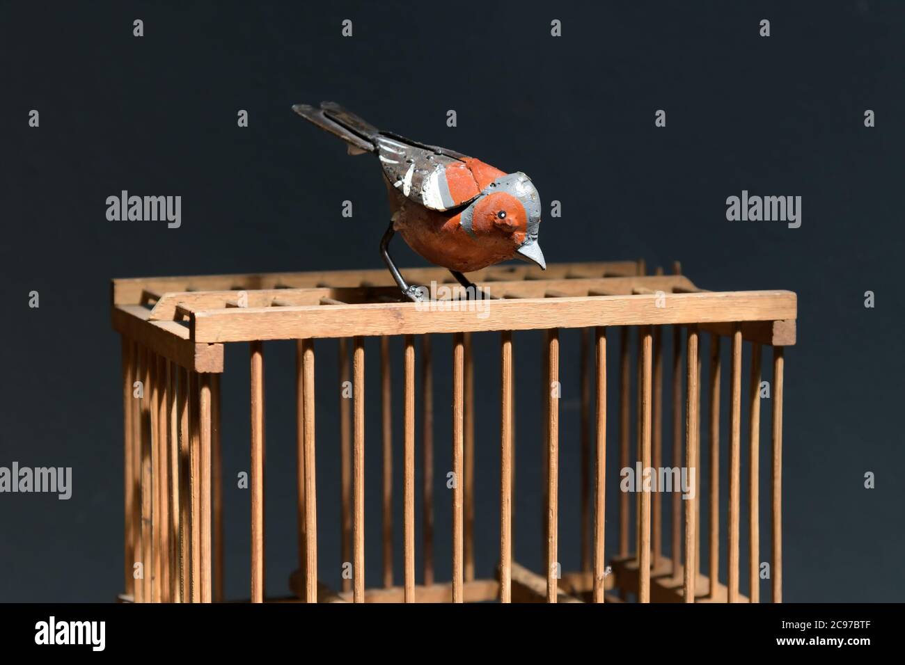 Bunte alte Vintage Metall oder Eisen Vogel auf einem Holzkäfig mit Bars Blick über die Seite in der Nähe über einem dunklen Hintergrund thront Stockfoto