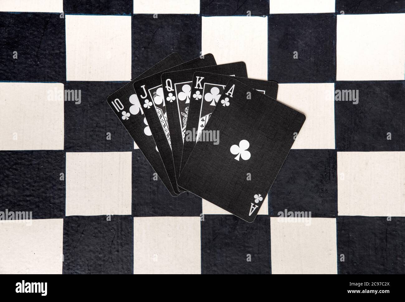 Royal Flush oder unschlagbar gewinnende Pokerhand in Vereinen auf schwarzen Karten auf einem Schachbrett, das von oben aus in einem flachen Lay gefächert wird Stockfoto