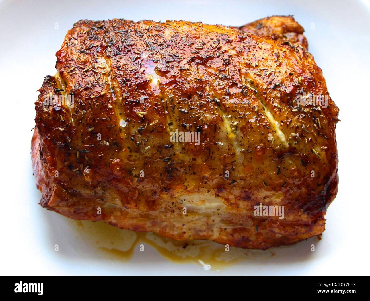 Schweinebraten in Olivenöl mit Thymian und Rosmarinkräutern direkt aus dem Ofen in einer weißen Keramikschale natürlich beleuchtet gekocht Stockfoto