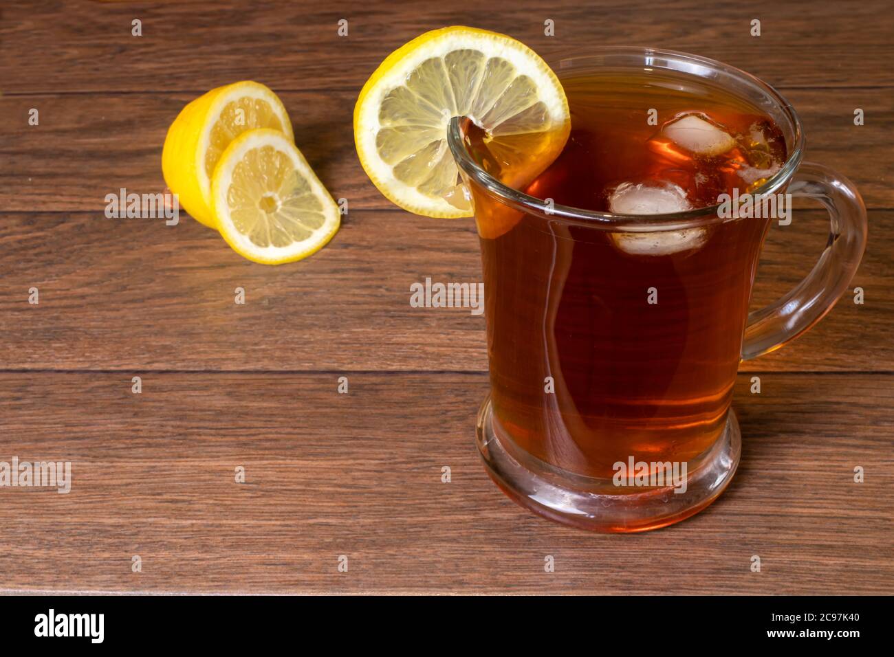 Schwarzer Tee mit Zitrone und Eis in einem transparenten Glas große Tasse auf einem braunen Holzhintergrund. Stockfoto