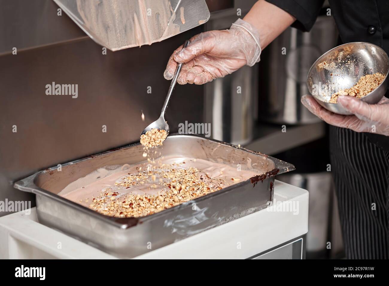 Herstellung von Eis - Eingießen von Nüssen in die Stahlpfanne mit Eis in der kleinen Fertigung - close up Stockfoto