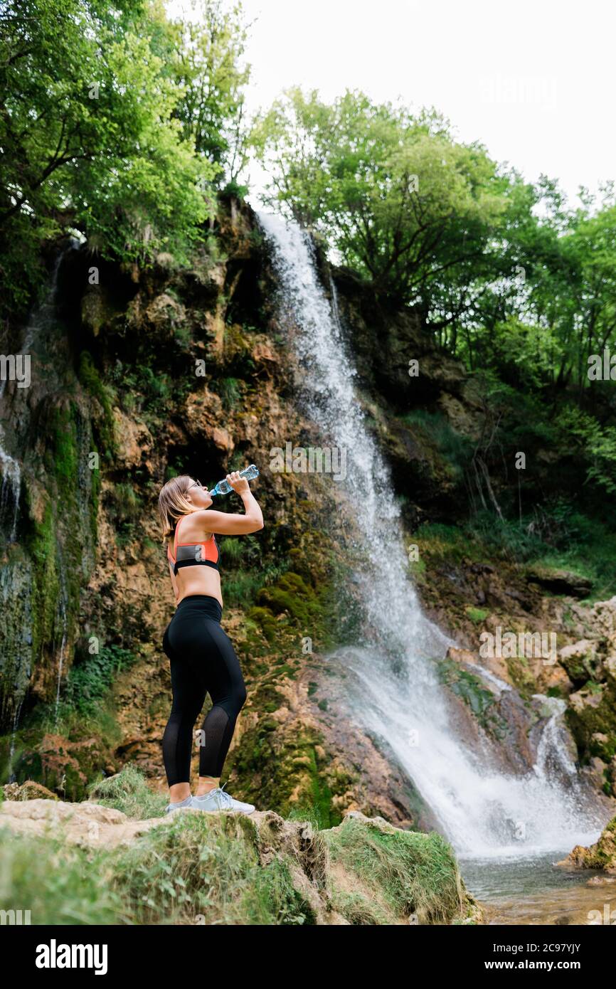 Junge weibliche Natur Entdecker Trinkwasser am Wasserfall Stockfoto
